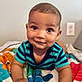 baby, child, smiling, striped_shirt, blanket, indoor, cute, playful, portrait, skin, face, hands, infant, young_child, happy, lying_down, colorful, patterned, room, electric_outlet
