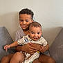Zeke joined the competition — help win amazing prizes! child, baby, sibling, smile, couch, indoor, hug, happy, family, person, toddler, curly_hair, short_hair, casual_clothing, wall, home, portrait, seated, cute, affection