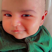 Muhammad is registered to the contest to win money with this photo: baby, infant, face, smile, green_clothing, closeup, skin, head, eyes, newborn, cute, child, person, soft_light, portrait, indoors, baby_clothes, expression, young_child, lying_down