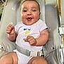 baby, smiling, onesie, baby_seat, happy, infant, chubby_cheeks, strapped, cute, child, face, hands, white_clothing, indoor, seatbelt, comfort, expression, closeup, young, person
