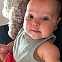 baby, child, face, eyes, tank_top, red_shorts, plush_toy, furniture, indoor, skin, arm, cute, infant, portrait, close_up, candid, expression, soft_lighting, comfort, casual_clothing