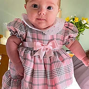 Freya joined the competition — help win amazing prizes! baby, child, pink_dress, plaid_pattern, bow, cute, portrait, indoor, flower_vase, yellow_flowers, white_flowers, soft_lighting, person_holding_child, face, wide_eyes, curious_expression, short_hair, collar, ruffled_sleeves, home_interior