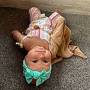Frankie is registered to the contest to win money with this photo: baby, infant, headband, bow, striped_clothing, carpet, blanket, floor, cute, child, portrait, indoors, looking_up, soft_toys, smiling, skin, person, comfortable, playtime, casual