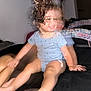 child, toddler, curly_hair, bow, blue_onesie, polka_dots, smile, barefoot, legs, indoor, bed, blur, motion, playful, infant, person, happy, skin, hand, foot