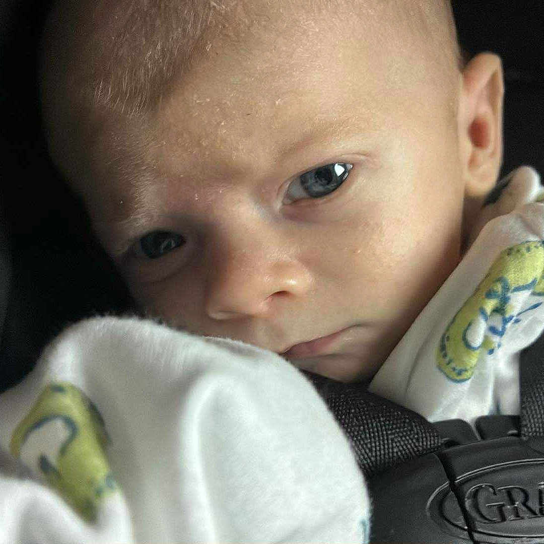 Orion is registered to the contest to win money with this photo: baby, blanket, car_seat, child, closeup, clothing, expression, eyes, face, graco, head, indoors, infancy, infant, person, portrait, seatbelt, sitting, soft, young