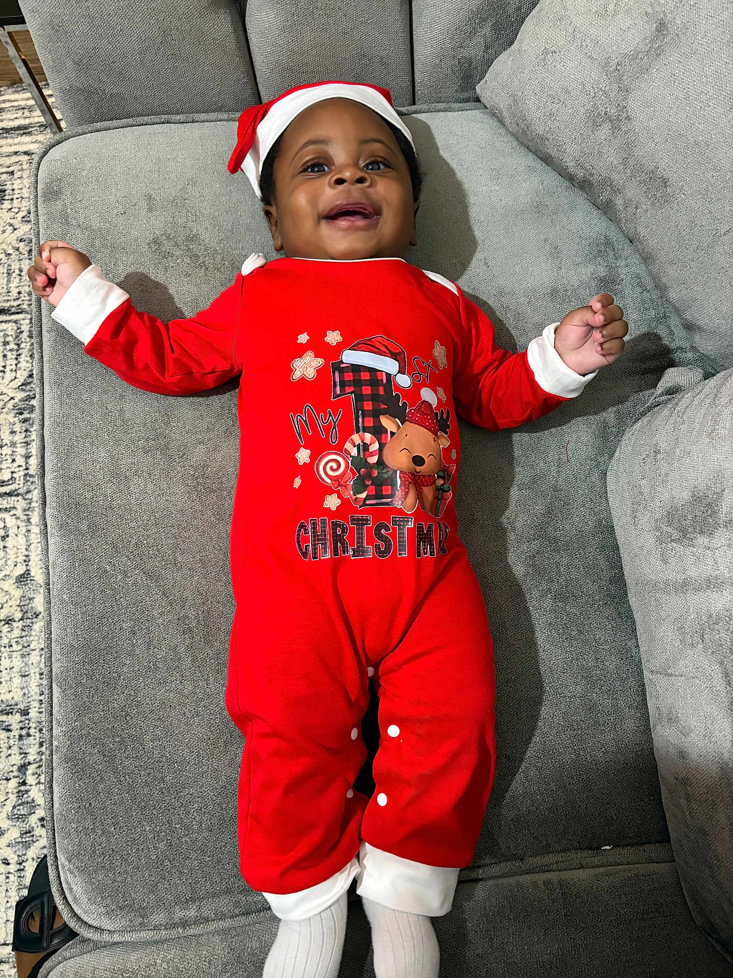 Uzziah joined the competition — help win amazing prizes! baby, child, smiling, christmas, holiday, onesie, red_clothing, hat, socks, couch, furniture, indoors, happy, portrait, infant, cute, cozy, celebration, festive, person