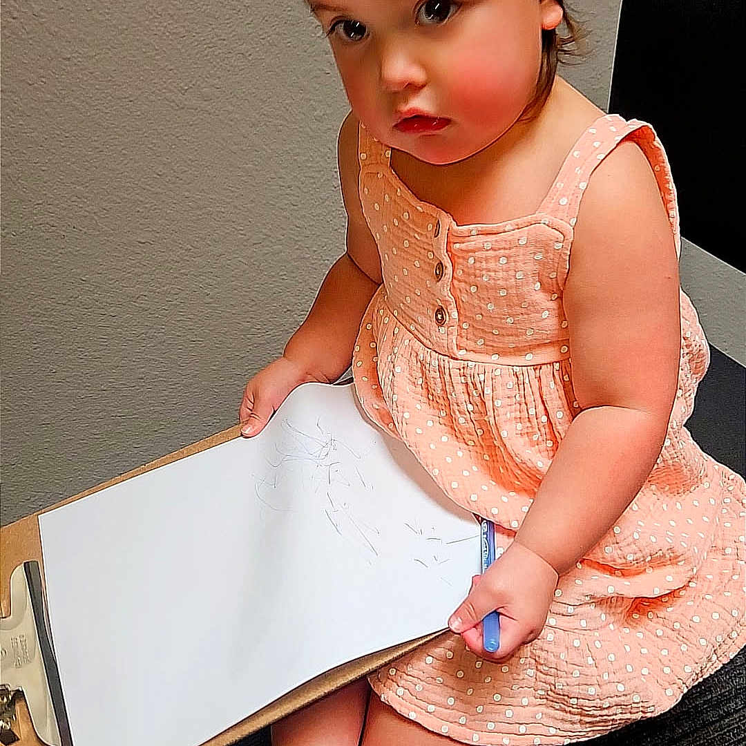 Amaya is registered to the contest to win money with this photo: toddler, child, girl, dress, headband, bow, clipboard, paper, pen, sandals, chair, indoor, floor, wall, sitting, cute, thoughtful, polka_dot, footwear, young