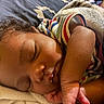 baby, sleeping, curly_hair, striped_shirt, blanket, close_up, peaceful, child, resting, soft_texture, indoors, cute, portrait, infant, skin, hand, face, young_child, cozy, nap