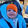 baby, child, smiling, blue_jacket, orange_hat, stroller, outdoor, water, wooden_dock, sunny, happy, face, person, winter_clothing, bundle_up, seatbelt, nature, daylight, cute, portrait