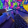 dog, white_dog, couch, leopard_print_pants, person, legs, underwater_theme, light_installation, mermaid, sea_creature, seahorse, coral, flower, glowing, colorful, indoor, art_installation, decorative_lighting, blue_lighting, relaxing