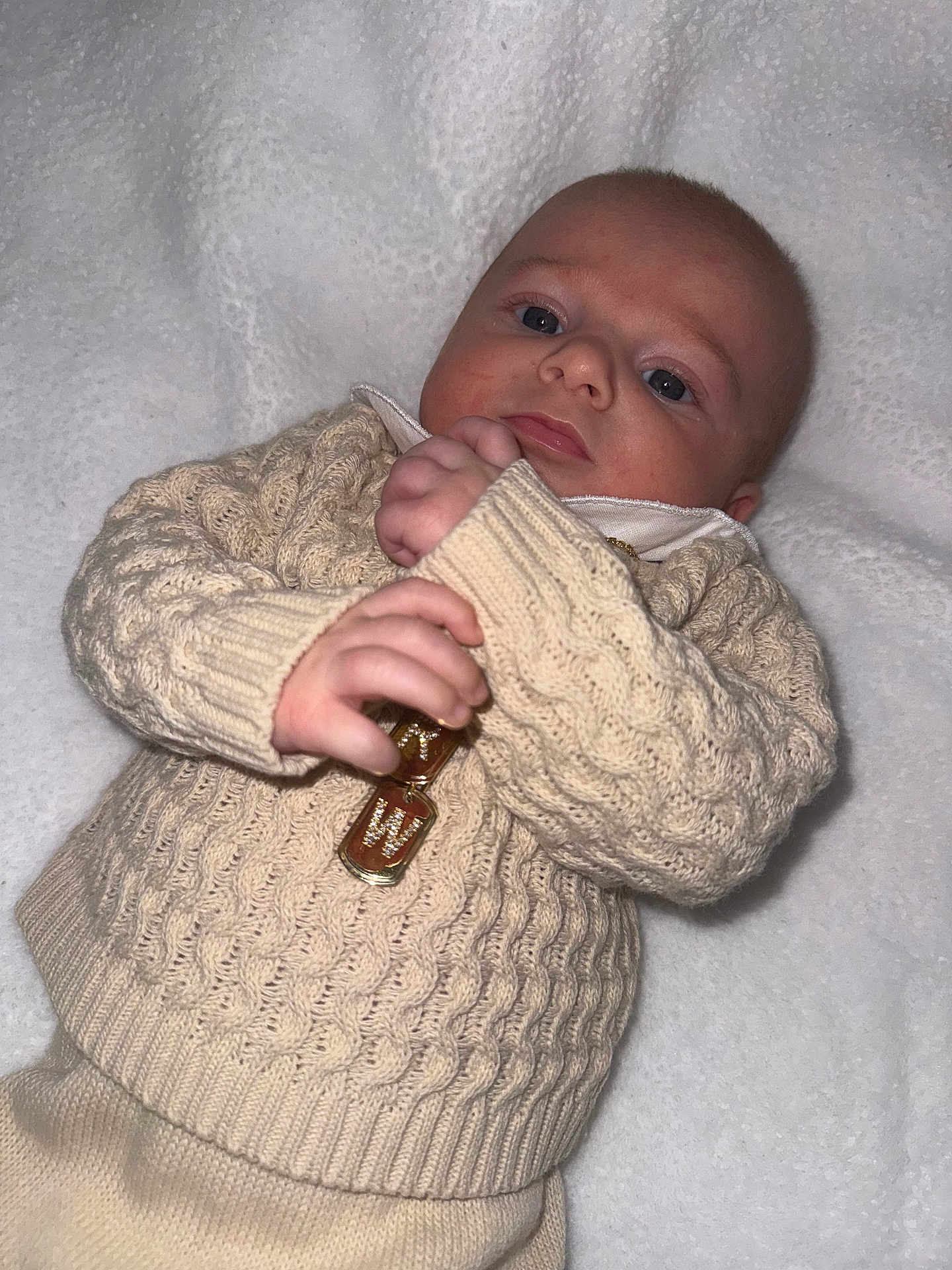 Richard is registered to the contest to win money with this photo: baby, infant, knitwear, sweater, cream_color, blanket, hand, face, portrait, cute, cozy, soft_texture, gold_pendant, lying_down, closeup, child, newborn, warm_clothing, indoors, person