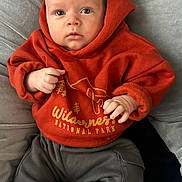 Jude joined the competition — help win amazing prizes! baby, infant, hoodie, orange_clothing, grey_pants, checkered_socks, cushion, soft_fabric, indoor, child, portrait, cute, cozy, sitting, hands, face, eyes, expression, comfortable, casual_clothing