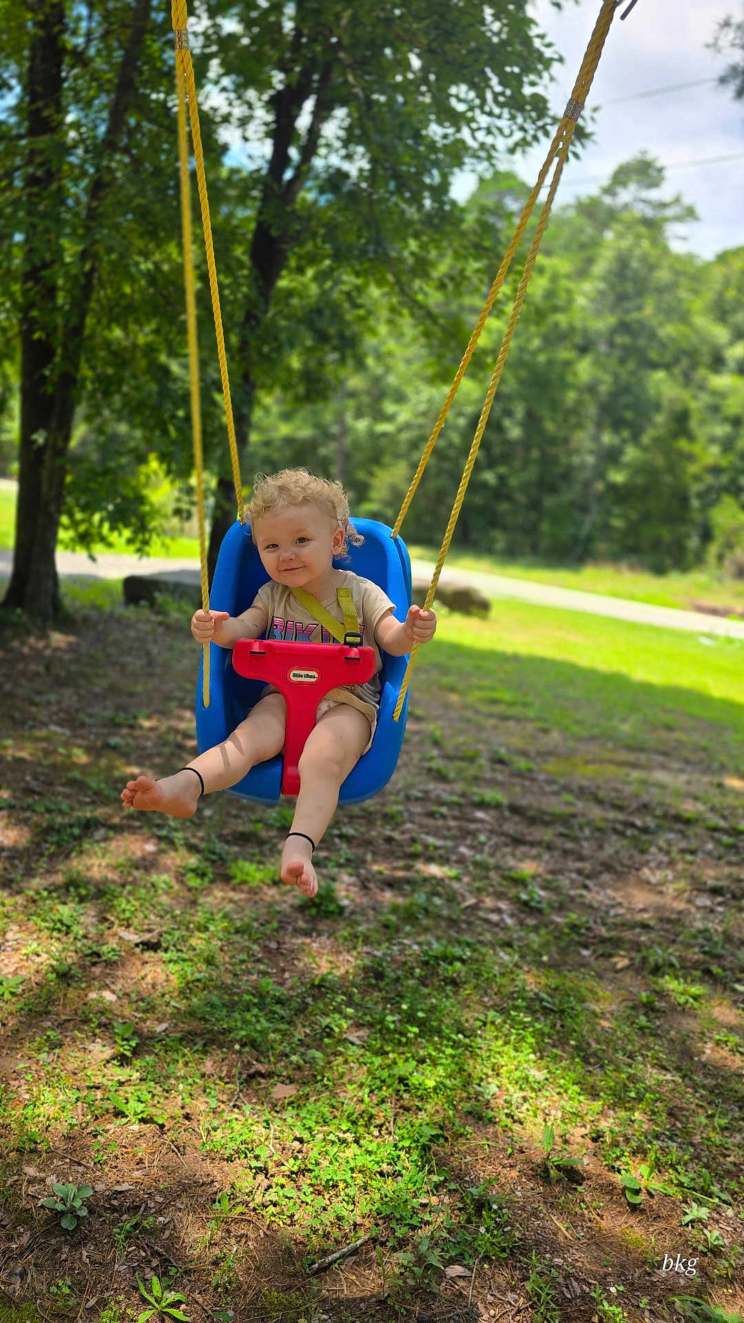 Aries joined the competition — help win amazing prizes! toddler, child, swing, outdoor, playground, trees, greenery, grass, sunlight, nature, smiling, blonde_hair, curly_hair, blue_swing, red_swing, barefoot, summer, park, happy, daytime