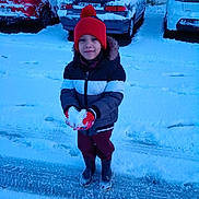 Djaymï a rejoint le concours — aidez-le/la à gagner de superbes lots ! child, snow, winter_clothing, hat, gloves, jacket, boots, parking_lot, car, snow_covered, outdoor, smiling, holding_snow, cold_weather, snowy_ground, red_hat, casual, standing, daylight, playful