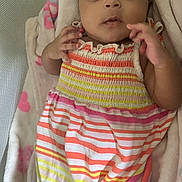 London is registered to the contest to win money with this photo: baby, infant, child, dress, striped_clothing, blanket, pink, yellow, orange, white, soft_texture, lying_down, cute, portrait, face, hands, curious, indoor, person, newborn