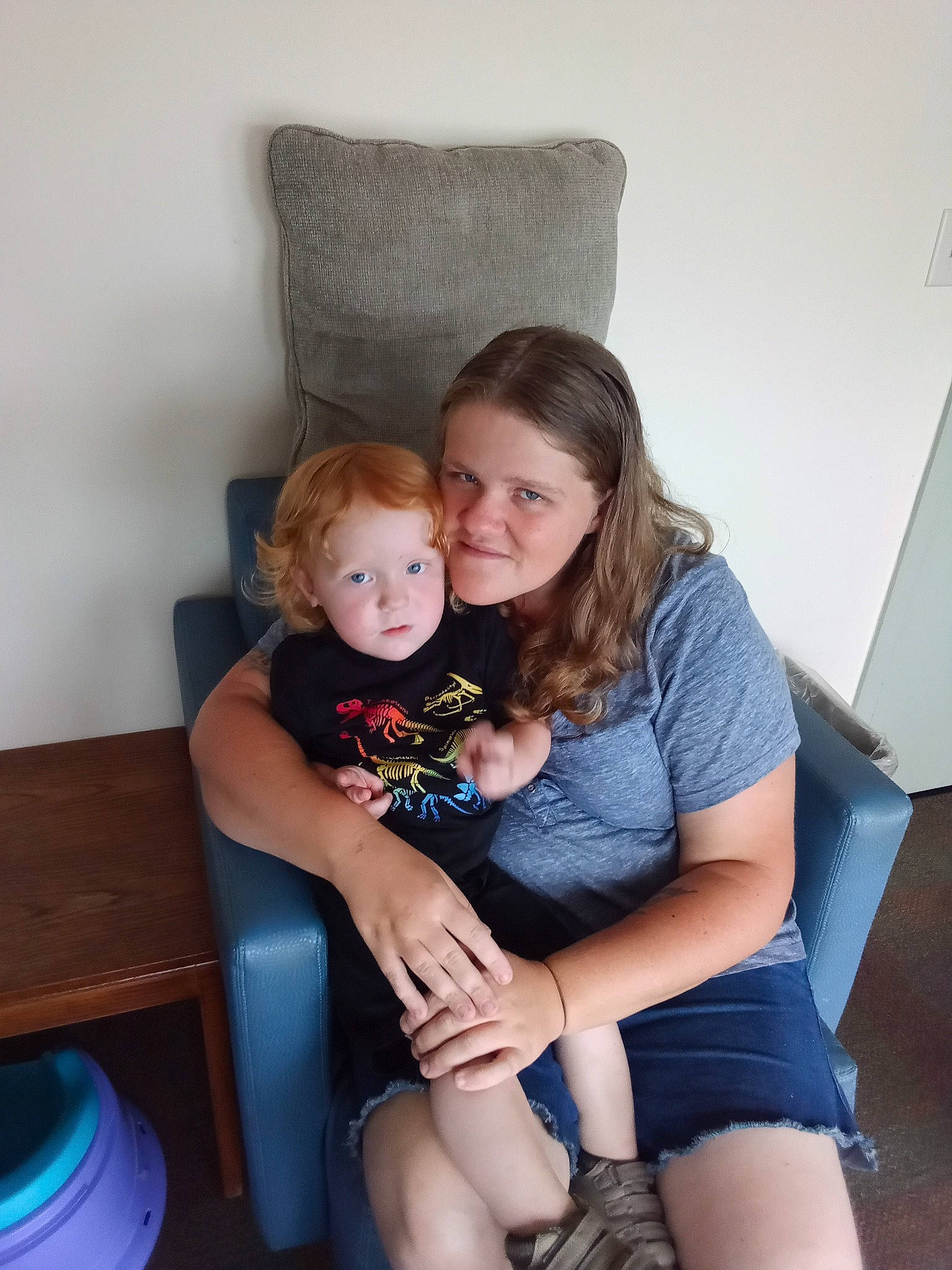 River is registered to the contest to win money with this photo: arm, blue, chair, clothing, comfort, facial_expression, fun, furniture, hairstyle, happy, joint, joy, knee, lap, leg, person, shorts, shoulder, skin, standing