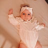 baby, infant, bed, onesie, headband, plush_toy, teddy_bear, lying_down, cute, child, soft_lighting, indoors, sleepwear, person, newborn, skin, legs, arms, white_clothing, expression