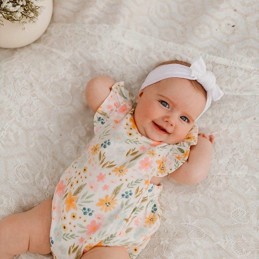 Baylyn joined the competition — help win amazing prizes! baby, infant, smiling, headband, floral_clothing, onesie, lying_down, blue_eyes, chubby, cute, lace_blanket, soft_texture, happy, portrait, child, indoors, peaceful, small_feet, adorable, comfort
