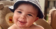 Cooper is registered to the contest to win money with this photo: baby, child, smile, hat, face, infant, cute, messy, chair, cushion, indoors, portrait, happy, skin, headwear, young, person, closeup, seat, expression