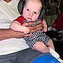 Hudson is registered to the contest to win money with this photo: baby, headphones, adult, hand, knee_brace, romper, sock, checkered_pattern, outdoor, night, chair, person, holding, face, blue, white, red, curious, seated, casual