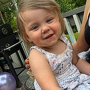 Liala is registered to the contest to win money with this photo: toddler, child, smiling, outdoor, porch, dress, floral_pattern, greenery, balloon, grill, summer, happy, person, nature, casual, tattoo, arm, daylight, family, relaxation