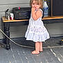 Liala joined the competition — help win amazing prizes! toddler, child, barefoot, dress, standing, porch, floor, table, stereo, spray_bottle, curious, finger_in_mouth, indoor, wooden_floor, household_items, clothing, person, young_child, expression, hair