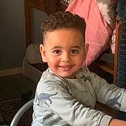 Outmane a rejoint le concours — aidez-le/la à gagner de superbes lots ! blanket, casual_clothing, chair, child, cozy, curly_hair, cute, dinosaur_print, face, furniture, happy, home, indoor, long_sleeve, person, portrait, sitting, smiling, table, young