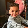 blanket, casual_clothing, chair, child, cozy, curly_hair, cute, dinosaur_print, face, furniture, happy, home, indoor, long_sleeve, person, portrait, sitting, smiling, table, young