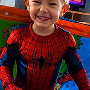 Liam participe au concours pour gagner de l'argent avec cette photo : child, smiling, spiderman_costume, indoor, toy_ball, blond_hair, television, animated_show, play_area, colorful, happy, person, young_child, costume, fun, portrait, standing, home, entertainment, bright_colors