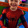 child, smiling, spiderman_costume, indoor, toy_ball, blond_hair, television, animated_show, play_area, colorful, happy, person, young_child, costume, fun, portrait, standing, home, entertainment, bright_colors