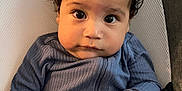 Tommy is registered to the contest to win money with this photo: baby, blue, child, clothing, cushion, cute, expression, eyes, face, hair, hand, indoor, infant, onesie, person, portrait, seat, sitting, skin, young