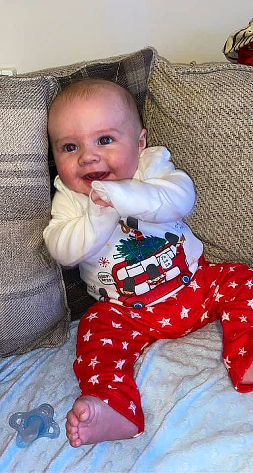 Zac is registered to the contest to win money with this photo: baby, baby_toddler_clothing, barefoot, cheek, child, comfort, couch, foot, home_accessories, human_body, lap, linens, living_room, nail, nightwear, pajamas, person, sitting, sock, thumb