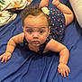 baby, infant, child, blue_dress, star_pattern, flower_hair_clip, curly_hair, lying_down, bed, blue_sheet, blanket, pillow, indoor, cute, chubby_cheeks, hands, face, eyes, skin, person