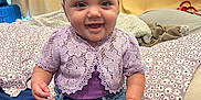 Milayshka is registered to the contest to win money with this photo: baby, child, smiling, sitting, clothing, jeans, cardigan, purple, bed, pillow, blanket, indoor, cute, happy, face, person, footwear, headband, curly_hair, infant