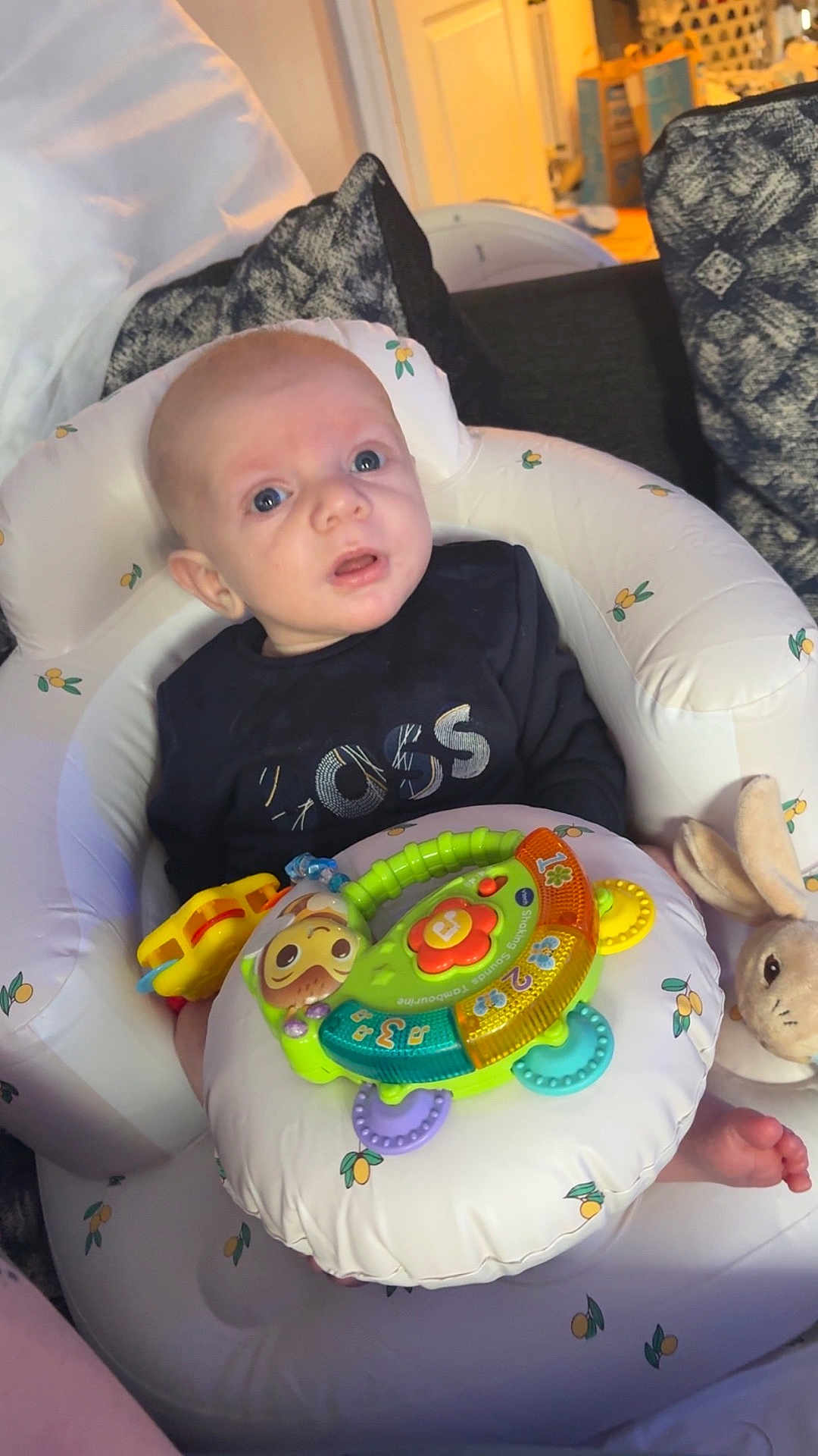 Taylor-Wayne is registered to the contest to win money with this photo: baby, inflatable_seat, toy, plush_bunny, cushion, blue_eyes, indoor, clothing, infant, child, face, person, furniture, comfort, curious, colorful, seat, home, relaxing, soft