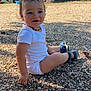 toddler, child, outdoor, playground, slide, gravel, sitting, white_clothing, sandals, happy, smiling, nature, greenery, sunlight, hair, necklace, bracelet, baby, person, daytime