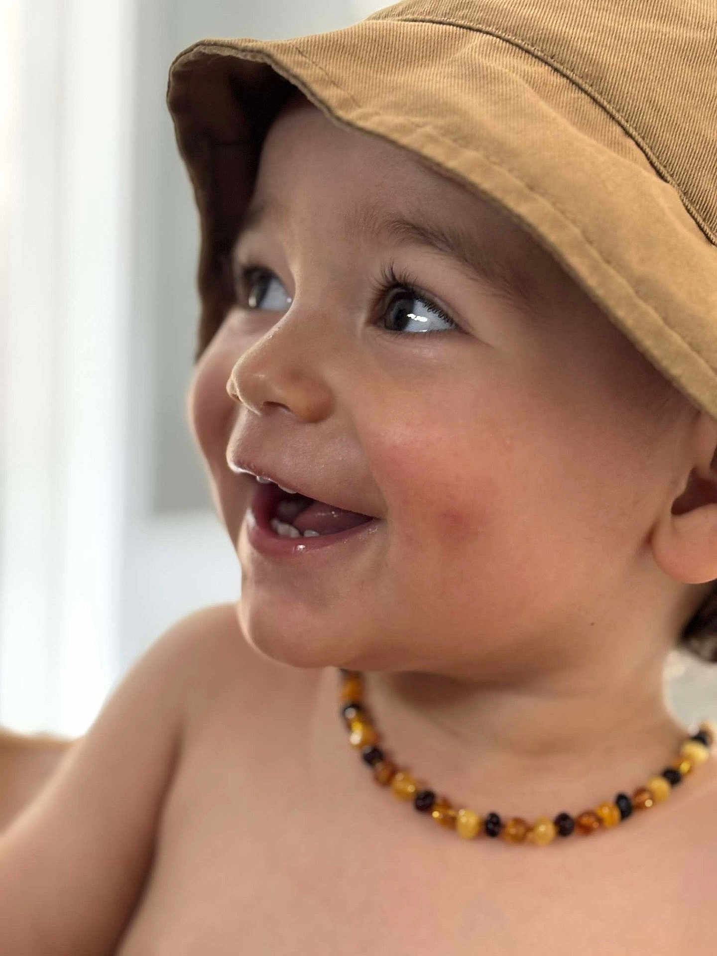 Tylio participe au concours pour gagner de l'argent avec cette photo : toddler, child, smiling, hat, bucket_hat, necklace, beads, face, portrait, closeup, happy, skin, expression, cute, young_child, indoor, person, headwear, jewelry, cheerful