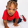 toddler, child, crawling, red_shirt, braided_hair, beads, sneakers, white_background, curious, cute, young_child, indoor, portrait, hands, face, smiling, clothing, feet, person, studio_photo