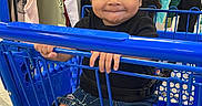 Sophia is registered to the contest to win money with this photo: baby, barefoot, black_shirt, blue_cart, child, clothing_rack, clothing_store, denim_shorts, happy, indoor, playful, portrait, retail, shopping, shopping_cart, sitting, smiling, store, toddler, tongue_out