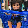 baby, barefoot, black_shirt, blue_cart, child, clothing_rack, clothing_store, denim_shorts, happy, indoor, playful, portrait, retail, shopping, shopping_cart, sitting, smiling, store, toddler, tongue_out
