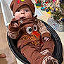 baby, infant, turkey_outfit, thanksgiving, brown_clothing, hat, kitchen, countertop, sink, decorations, christmas_tree, lights, festive, socks, striped_sleeves, baby_face, cute, indoors, holiday, black_basin