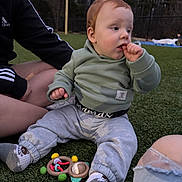 Hunter joined the competition — help win amazing prizes! baby, infant, toddler, child, sitting, outdoor, grass, toy, rattle, hoodie, socks, pants, red_hair, hand_in_mouth, park, adult_arm, dusk, playtime, casual_clothing, portrait