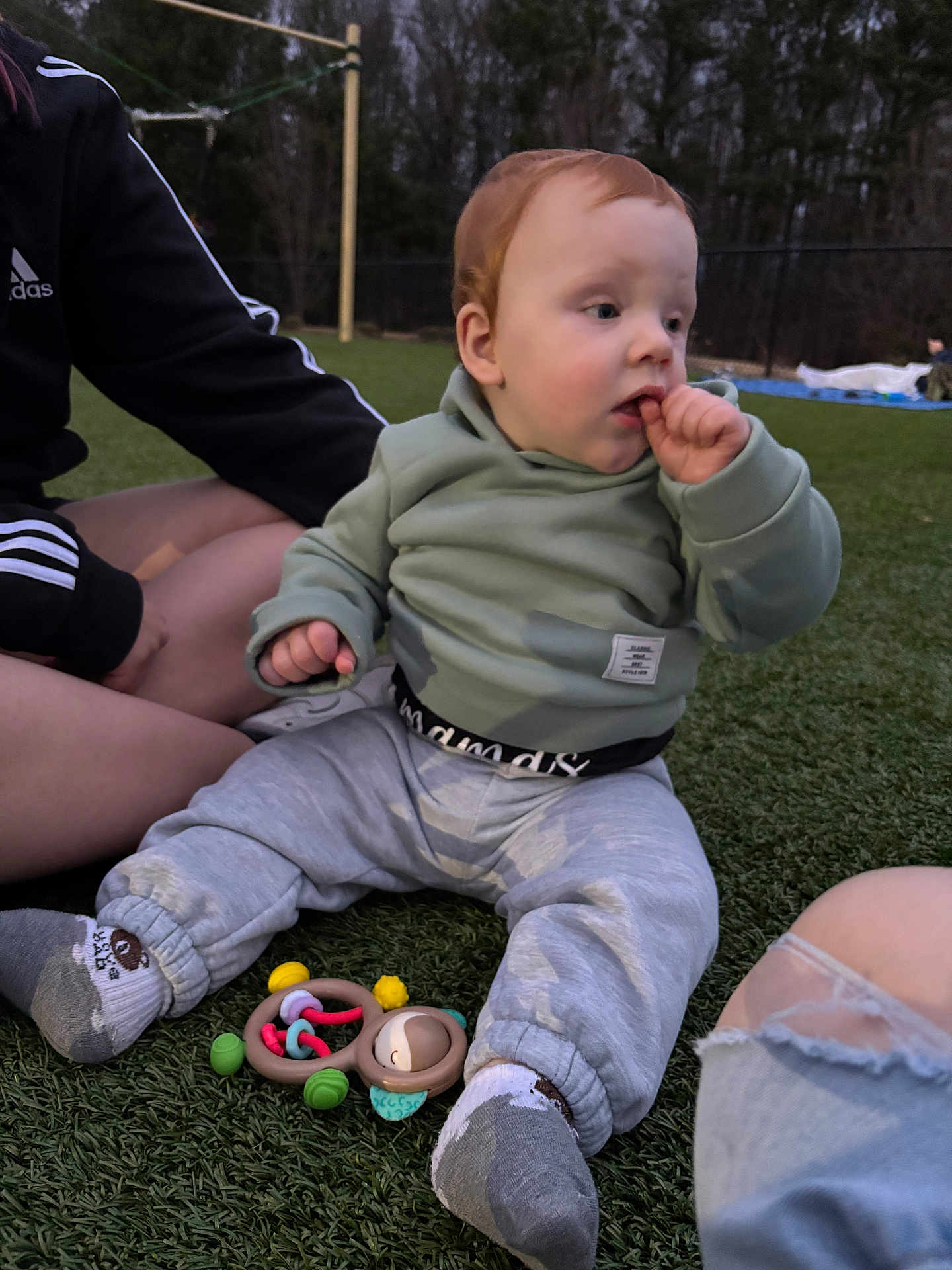Hunter joined the competition — help win amazing prizes! baby, infant, toddler, child, sitting, outdoor, grass, toy, rattle, hoodie, socks, pants, red_hair, hand_in_mouth, park, adult_arm, dusk, playtime, casual_clothing, portrait