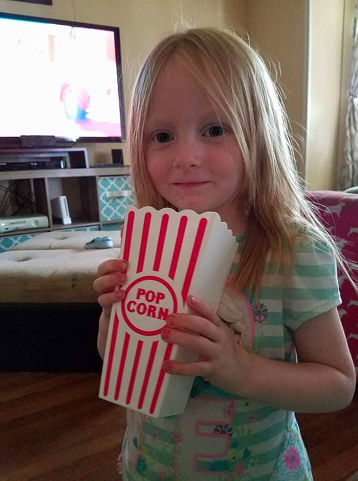 Kaylinn is registered to the contest to win money with this photo: blond, cable_television, child, computer_monitor, curtain, drink, drinkware, entertainment_center, finger, fun, happy, pattern, person, play, smile, standing, t_shirt, television, television_set, thumb