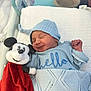 newborn, baby, sleeping, blue_clothing, knit_hat, mickey_mouse, plush_toy, blanket, hospital_bassinet, cute, infant, soft_texture, peaceful, child, toy, bed, cozy, smiling_face, resting, indoors