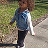 child, toddler, curly_hair, denim_vest, long_sleeve_shirt, pants, sneakers, sidewalk, outdoor, grass, trees, sunny, shadow, walking, nature, casual_clothing, person, daylight, park, young_child