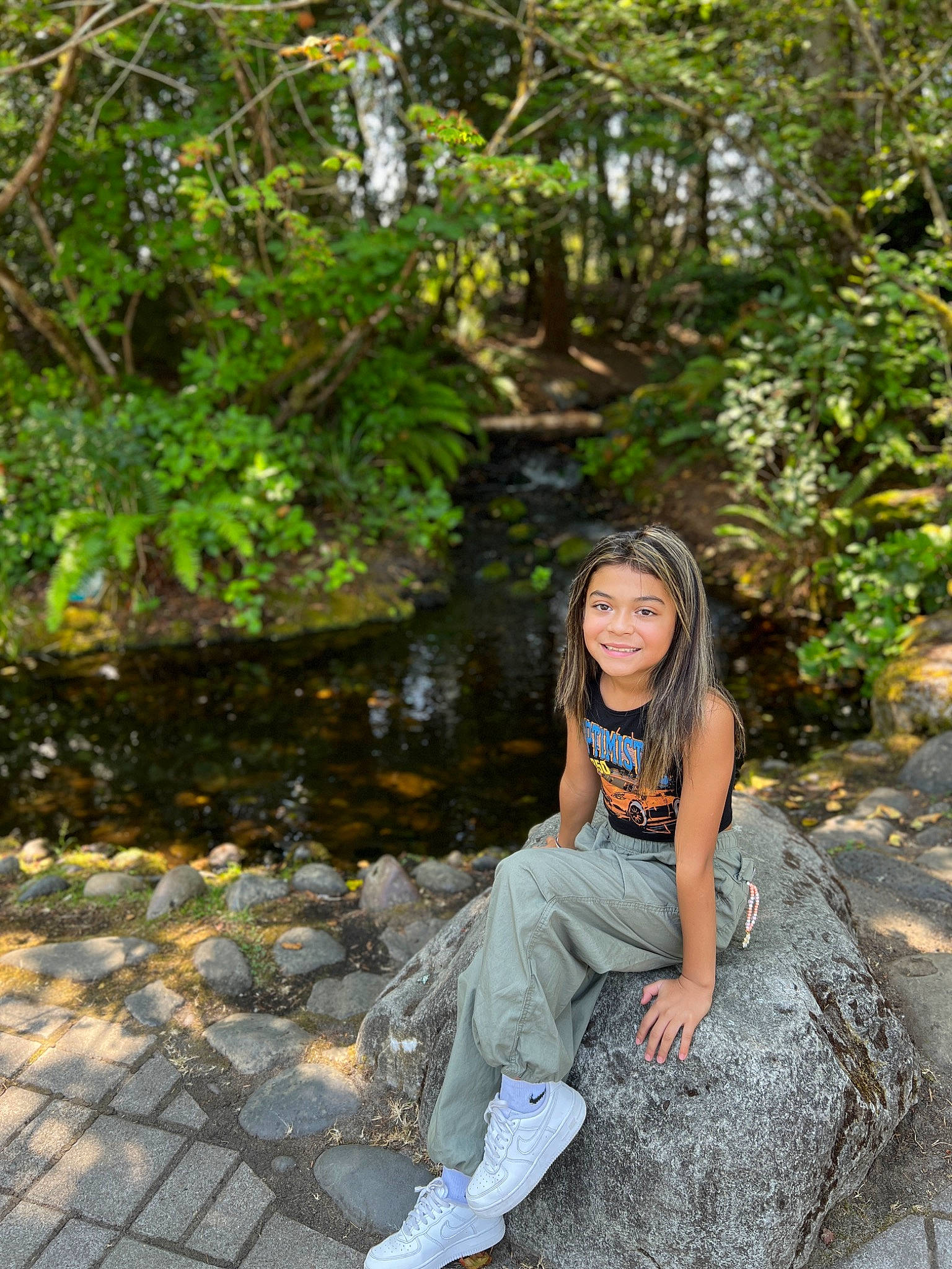 Denise is registered to the contest to win money with this photo: child, forest, garden, grass, happy, joy, jungle, landscape, leisure, people_in_nature, person, plant, recreation, rock, sitting, smile, soil, stream, toddler, tree