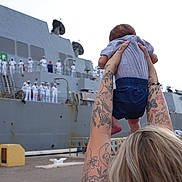 Grayson joined the competition — help win amazing prizes! baby, tattoos, adult, arms, naval_ship, sailors, uniforms, military, harbor, dock, outdoor, person, back_view, holding, child, tattooed_arms, crowd, gray_ship, blue_shorts, gray_shirt