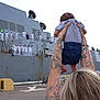 baby, tattoos, adult, arms, naval_ship, sailors, uniforms, military, harbor, dock, outdoor, person, back_view, holding, child, tattooed_arms, crowd, gray_ship, blue_shorts, gray_shirt