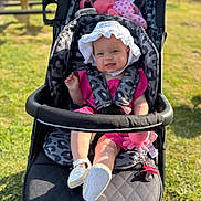 Lottie is registered to the contest to win money with this photo: baby, stroller, outdoor, sunhat, pink_clothing, smiling, grass, toy, pacifier, child, happy, seatbelt, footwear, sunlight, infant, cute, playful, patterned, person, daylight